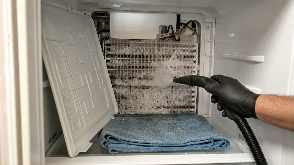 A freezer compartment with the rear panel off, evaporator fins packed with frost, the defrost heater exposed