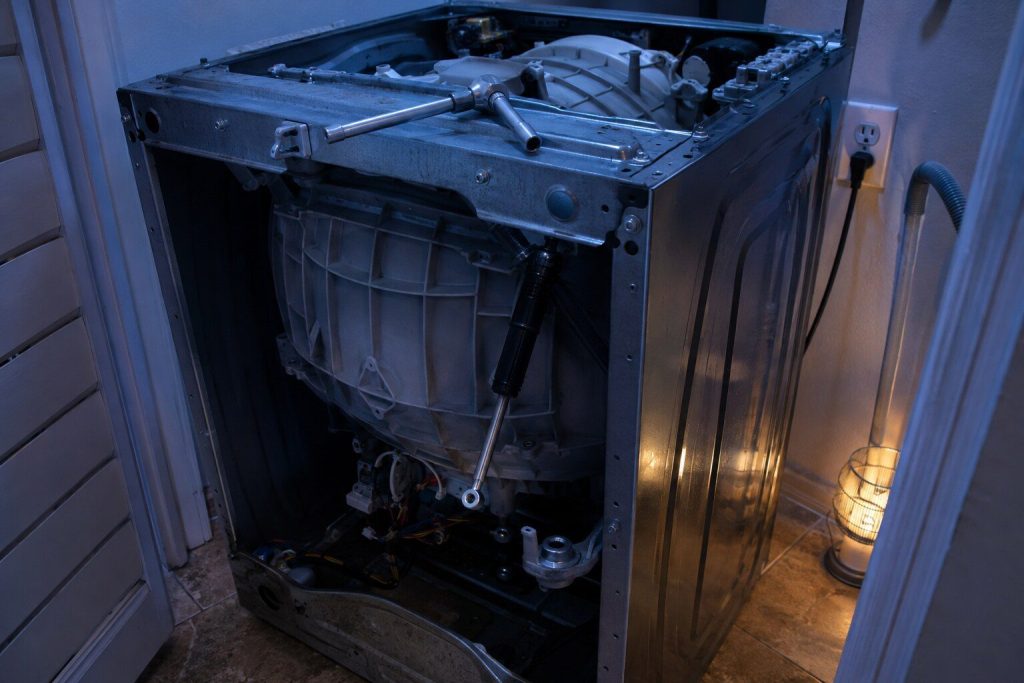 A washer with its top and front off and one suspension rod unbolted at the lower mount and swung clear