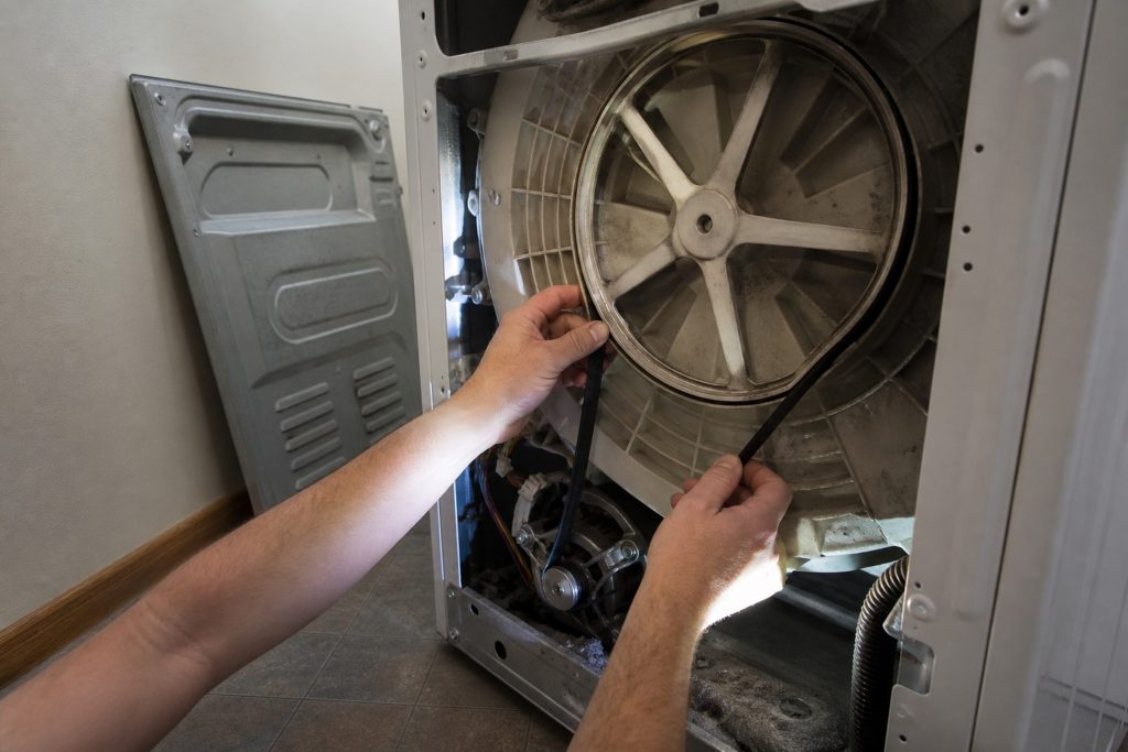 The rear panel of a washing machine removed and the drive belt looped around the motor pulley